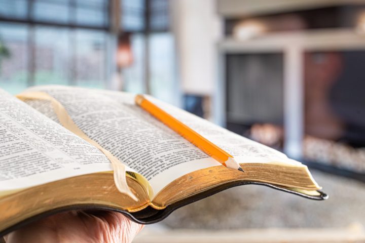 A man holds a Bible with a pencil, against the background of the living room.